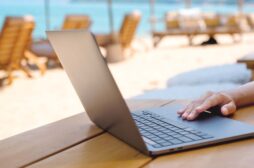 Laptop on beige table outside with beach and beach chairs behind