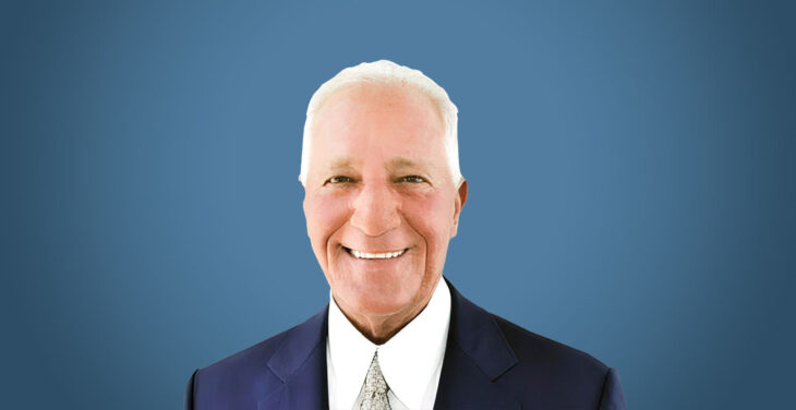 Headshot of Terry Gilmore on blue background with dark suit and light shirt