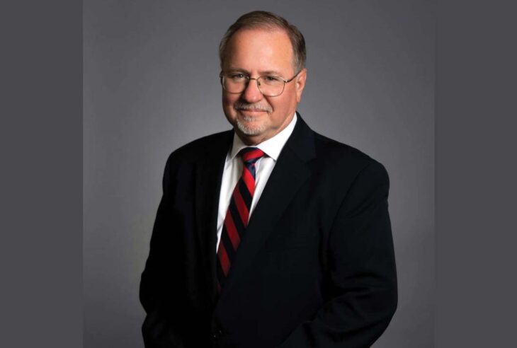 Lawyer wearing dark suit and red and blue tie against gray backdrop