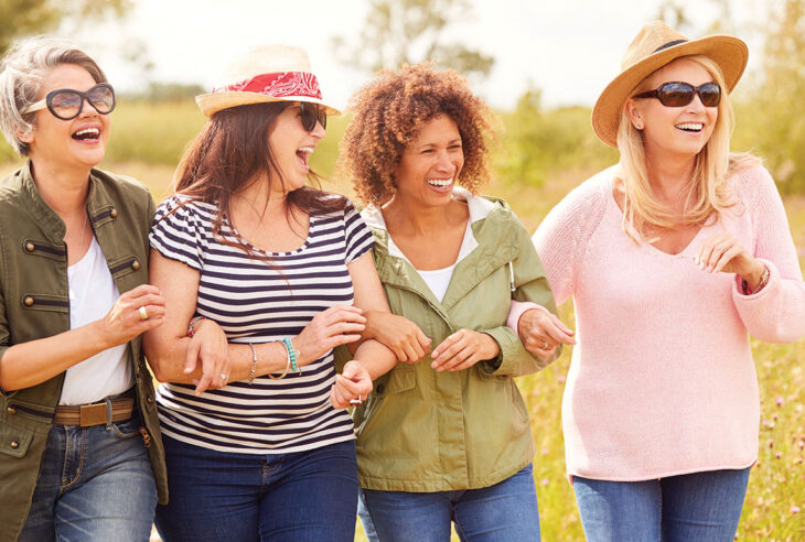 Four women walking outdoors with linked arms and smiling