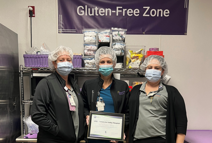 Three women wearing masks holding an award below sign that says gluten-free zone